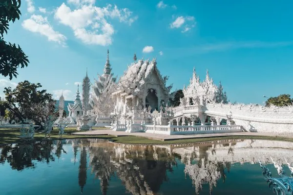 The White Temple reflected in water beneath a blue sky near Chiang Rai