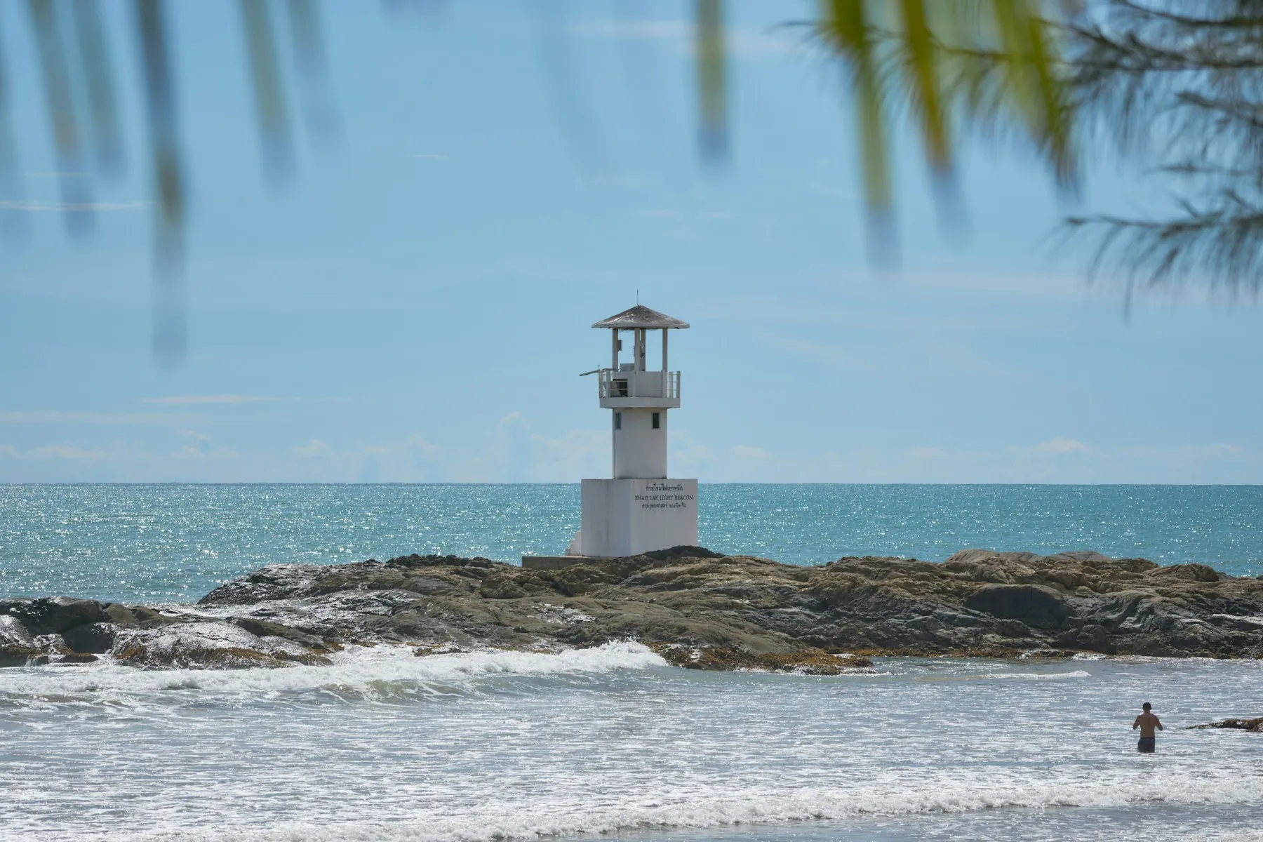 The white lighthouse on the rocks off Nang Thong Beach in Khao Lak, framed by foliage