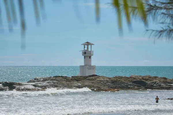 The white lighthouse on the rocks off Nang Thong Beach in Khao Lak, framed by foliage