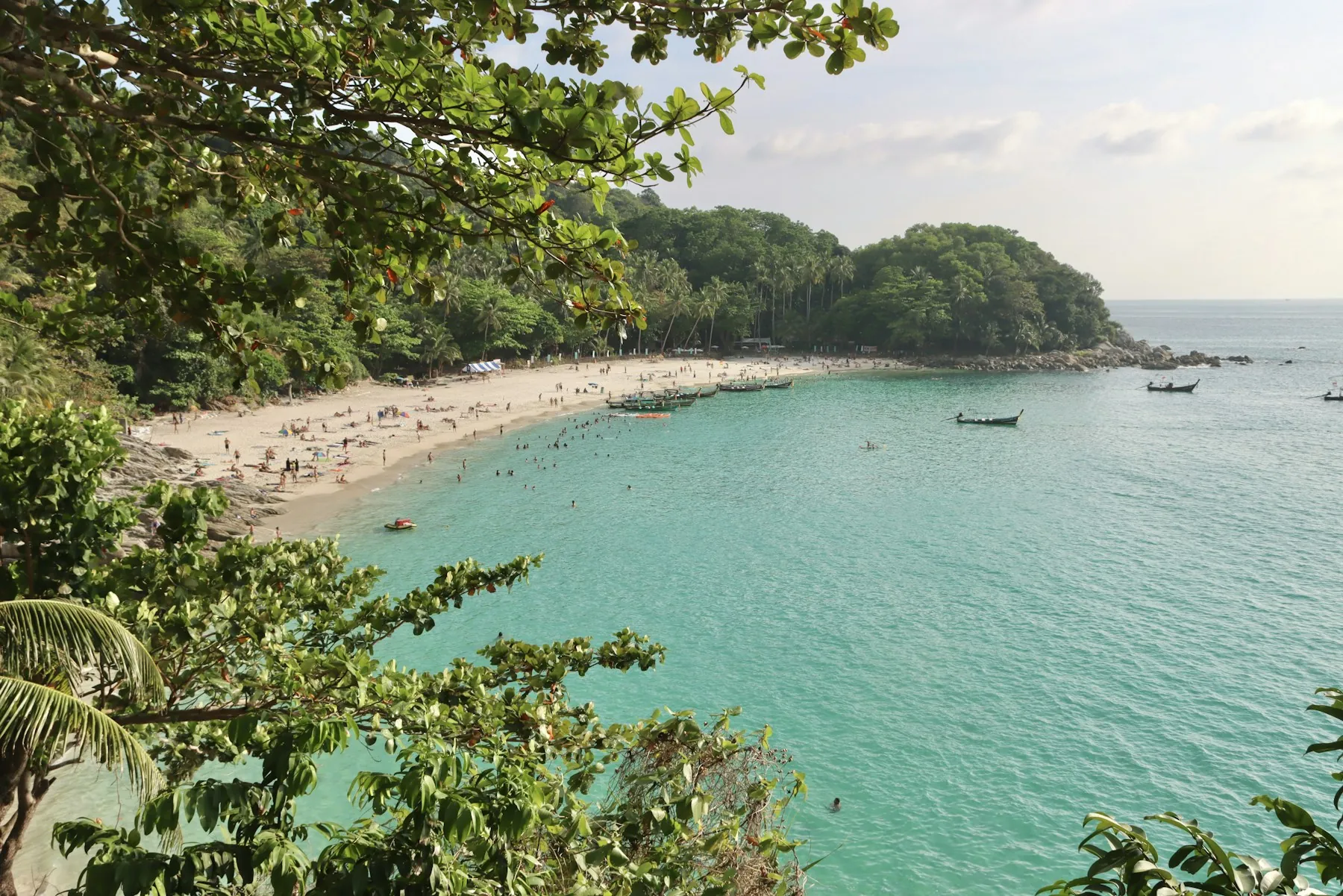 Freedom Beach on Phuket, framed by tropical foliage with swimmers and longtail boats in the bay