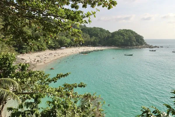Freedom Beach on Phuket, framed by tropical foliage with swimmers and longtail boats in the bay