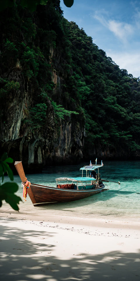 A longtail boat beside white sand and clear turquoise water in the Phi Phi Islands