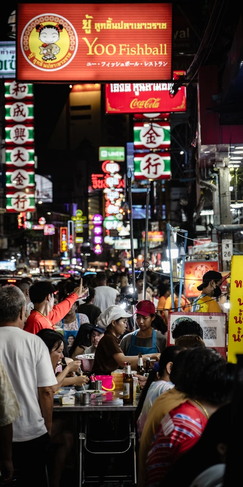 Diners eating at street tables beneath illuminated signs in Bangkok Chinatown