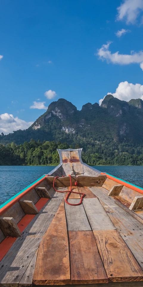 A longtail boat pointing toward forested limestone mountains across a lake